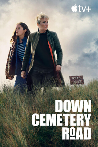 filmplakat für die serie „down cemetery road“ auf apple tv. zwei frauen stehen auf einer grasbewachsenen anhöhe mit einem verwitterten schild im hintergrund. sie blicken in die ferne, gekleidet in lässige jacken vor einem bewölkten himmel.
