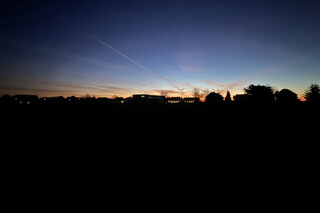 sonnenaufgang in karken mit kahlen bäumen und häuser-silhouetten am horizont. der himmel leuchtet blau-orange.