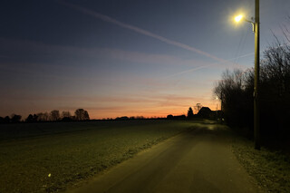 strasse in karken imorgengrauen mit einem strassenlicht. man sieht den orange-blauen morgenhimmel.