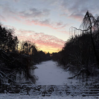foto des zugefrorenen möwensee beim morgenspaziergang. im hintergrund leuchtet der himmel orangeblau