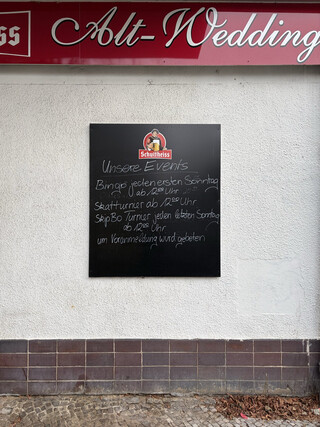 schild an der fassade der „alt-wedding“ gaststätte. es wird um „voranmeldung“ für „Unser Events“ gebeten (Bingo, jeden ersten Sonntag, ab 12:00 Uhr, Skatturnier ab 12:00 Uhr, SkipBo Turnier jeden letzten Sonntag ab 12:00 Uhr)