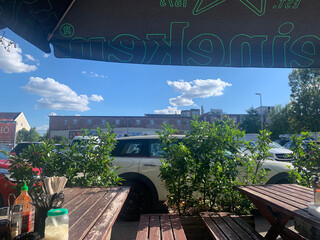 blick vom aussenbereich des duc anh quan restaurant auf den parkplatz. im vordergrund stehen pflanzen, im hintergrund der blaue himmel mit weißen wolken.